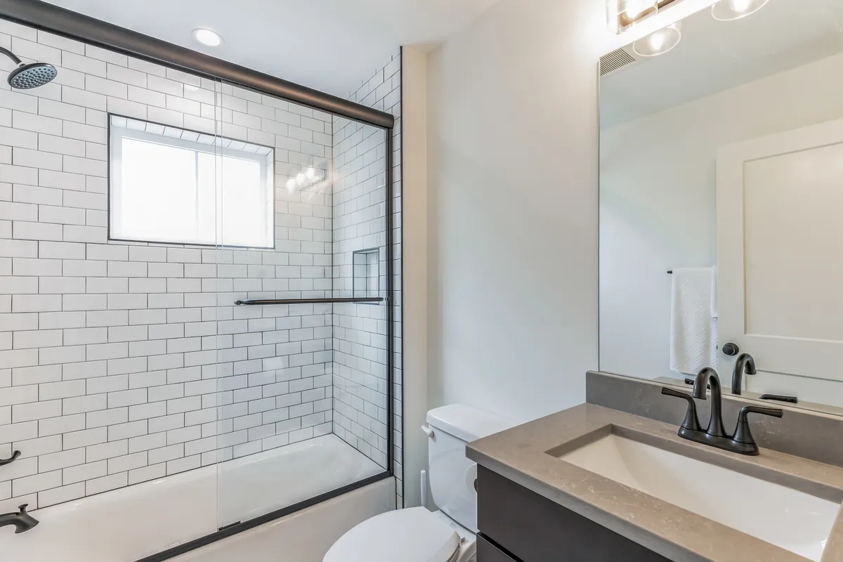 A bright bathroom featuring a spacious shower area, sink, and mirror. The design is simple yet modern, offering a refreshing and tranquil atmosphere ideal for self-care.