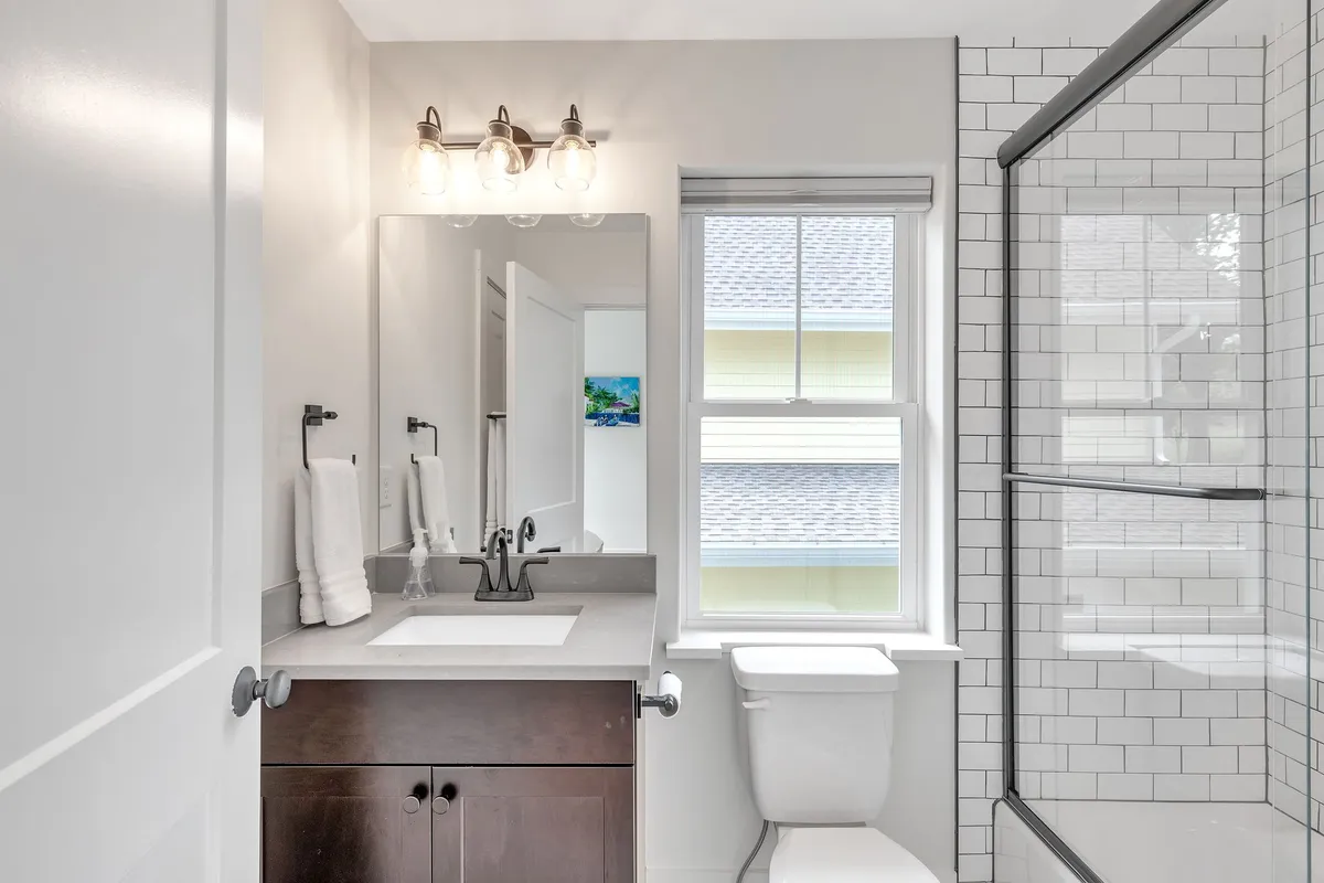 A modern bathroom scene with a vanity and sink, glass-enclosed shower area, mirror, and a window for natural light. The space is fresh, clean, and inviting—an ideal spot for daily routines and moments of solitude.
