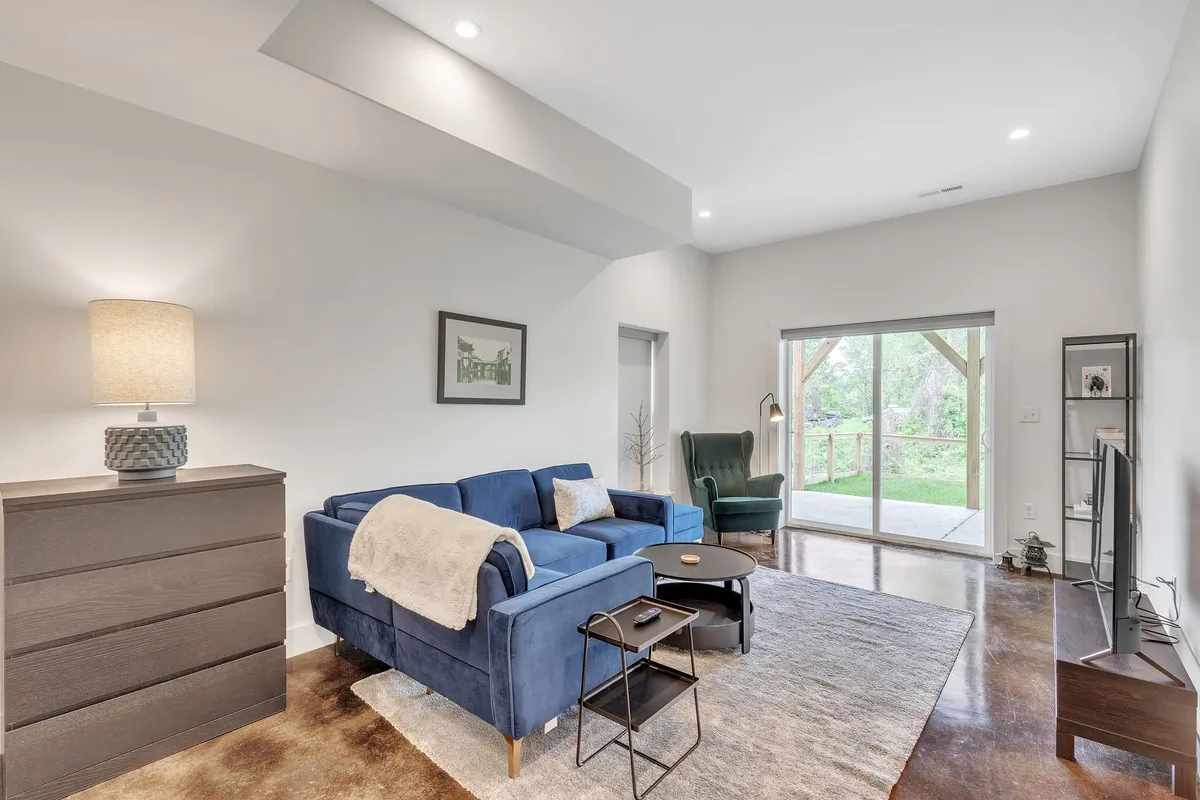 A modern living area with a blue sectional sofa, wooden coffee table, and large sliding doors that open onto a sunlit deck. The setup invites both indoor relaxation and easy access to the outdoors, with natural light enhancing the cheerful, open feel.