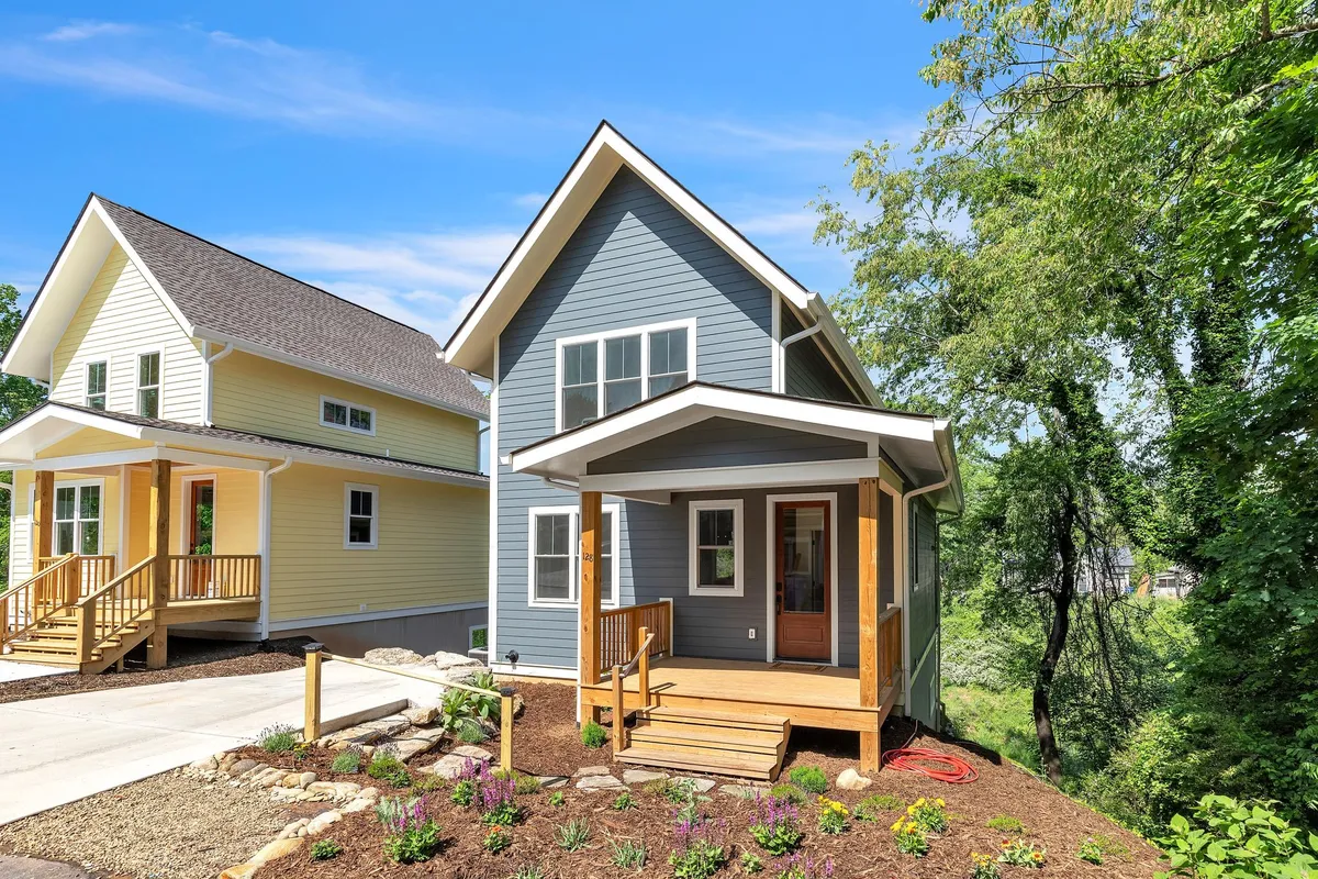 The image shows a welcoming blue house with a spacious porch and a landscaped garden. The porch is ideal for relaxing or working outdoors, surrounded by lush greenery that hints at the tranquil neighborhood setting. The home conveys a sense of comfort and connection to nature, with ample space for both work and leisure.