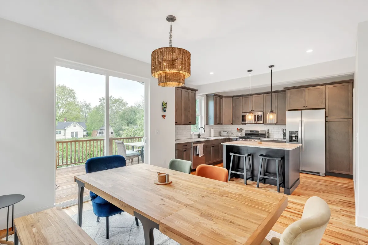 A bright, open-plan view showing a kitchen island, dining table, and large windows that flood the space with natural light. The scene highlights the seamless connection between the kitchen and adjacent living areas.