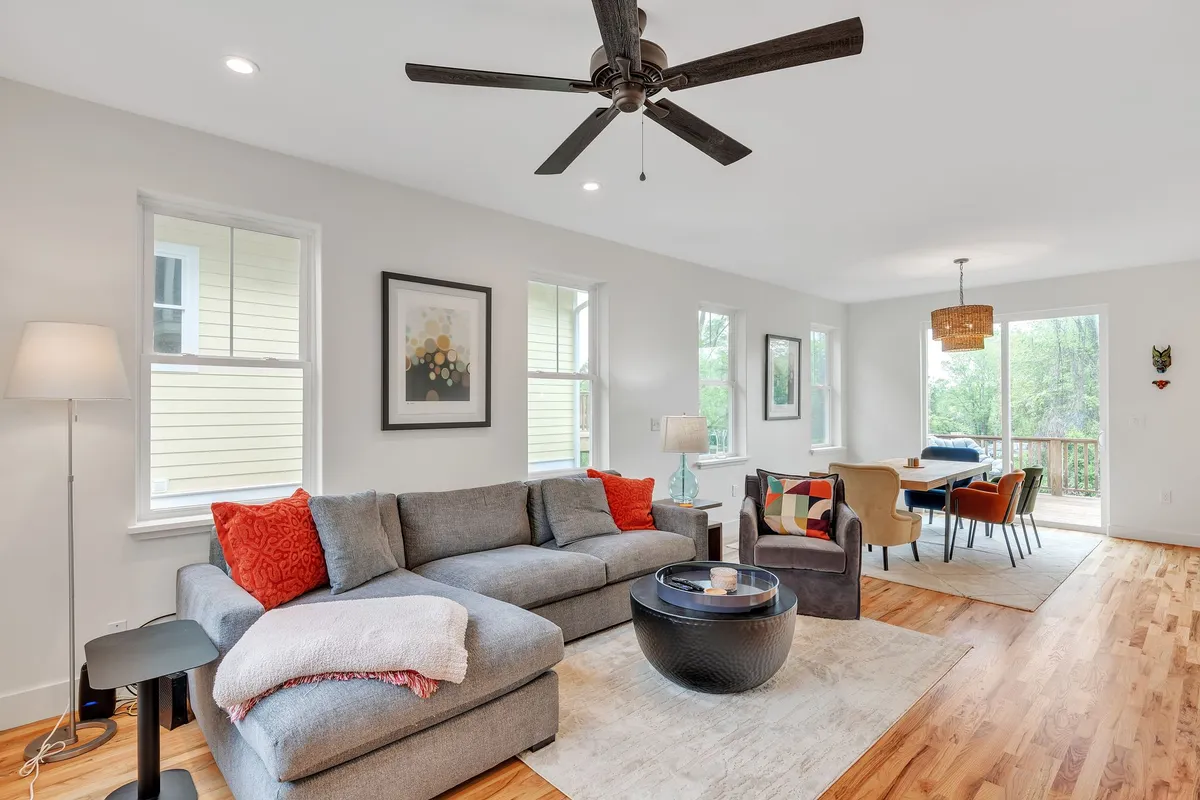 A comfortable interior scene with a sofa, dining table, ceiling fan, and vibrant artwork on the walls. The arrangement encourages socializing and family gatherings, with ample space for both relaxation and shared meals.