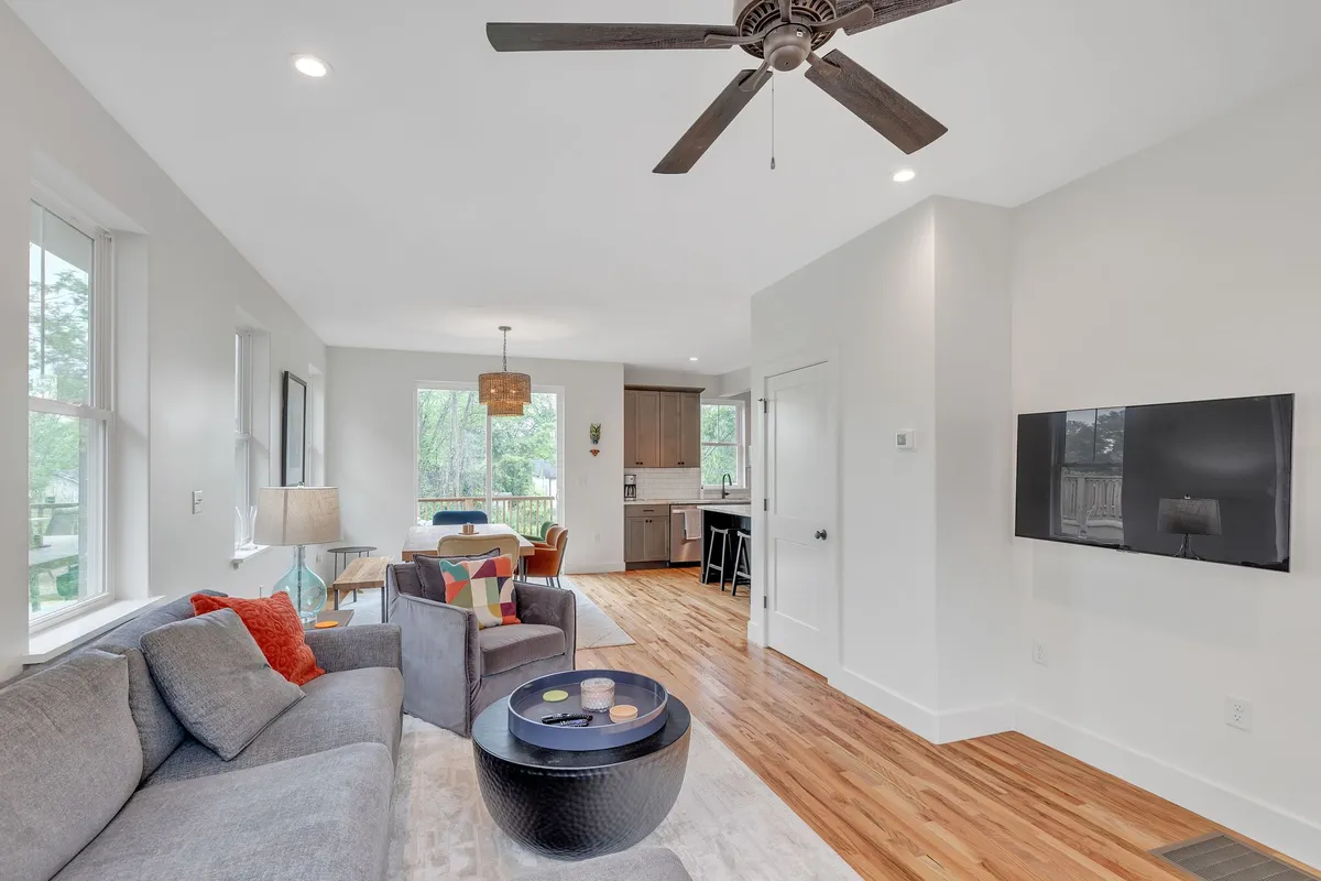 A welcoming interior scene centered on a cozy gray sofa with colorful accent pillows and a wooden coffee table. The space is open and inviting, ideal for relaxing or socializing after a productive day.