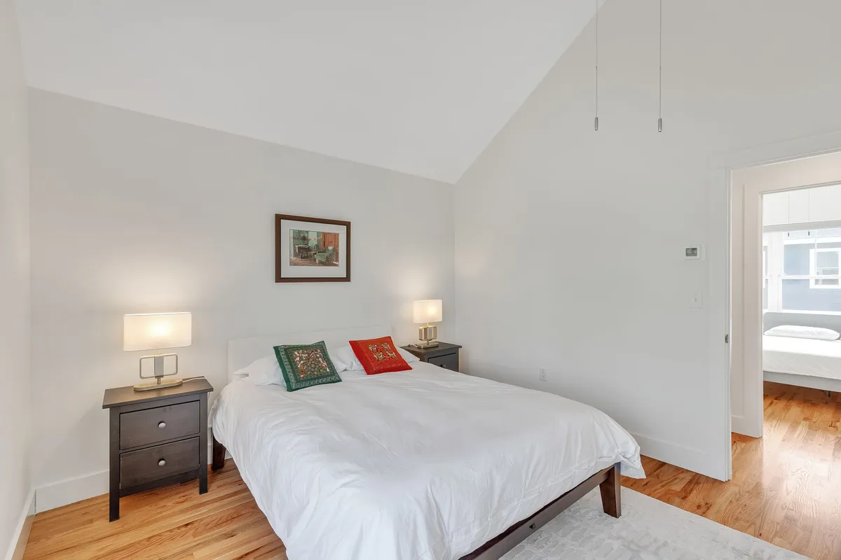 A bedroom arranged with a neatly made bed featuring decorative pillows, nightstands flanking the bed, each with a lamp, and framed artwork on the wall. The mood is relaxing and peaceful, with sunlight streaming in to enhance the sense of warmth and privacy.