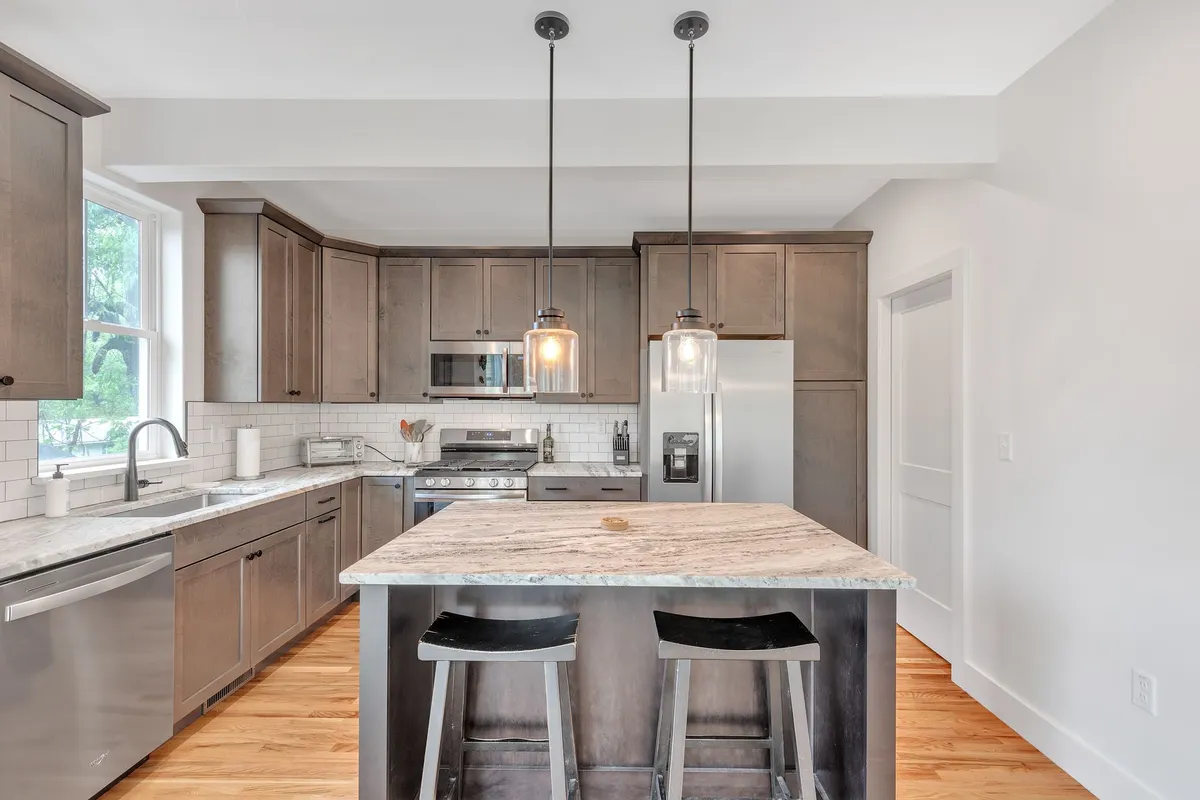 A large kitchen island stands at the center, accentuated by stylish pendant lighting and flanked by high-end stainless steel appliances. The layout prioritizes both functionality and a comfortable atmosphere for entertaining.