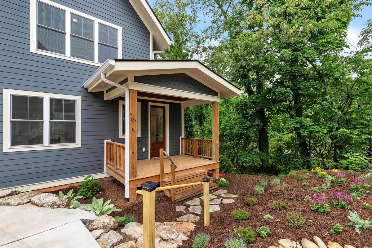 An inviting exterior shot of a porch and front door framed by a landscaped garden. The porch is welcoming, perfect for morning coffee or evening chats, with greenery providing a sense of privacy and immersion in nature.